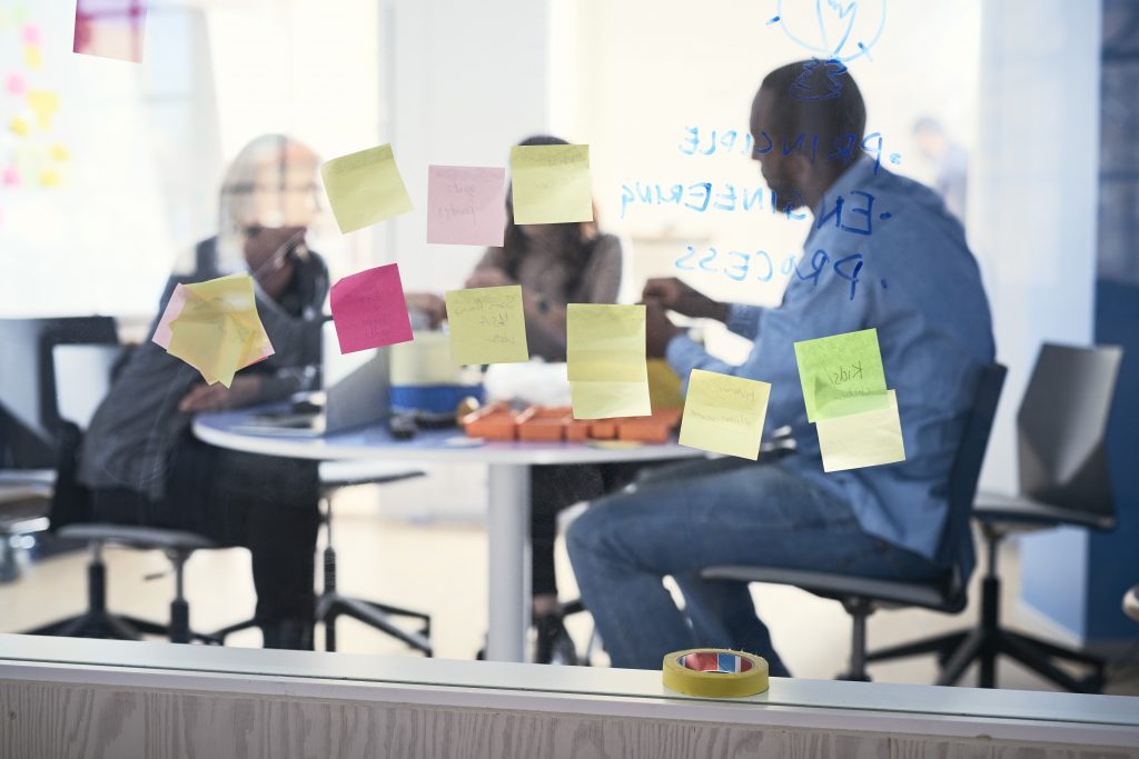 Collaborative team working in a meeting room at Openlab behind a window with post-it notes on.